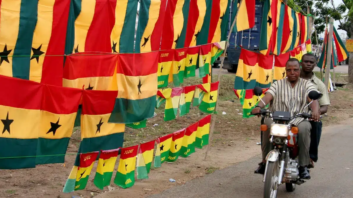 Men riding on a motorbike with Ghana flags in the background