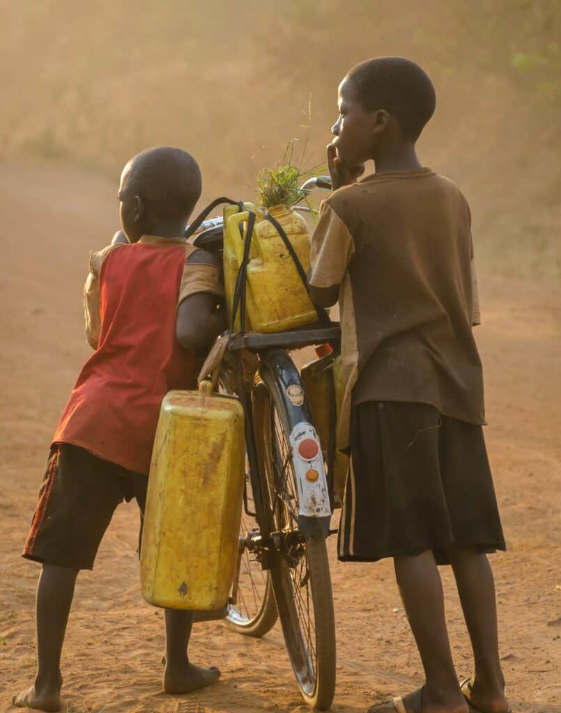Children going to fetch water with gallons on a bicycle